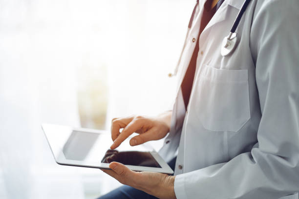 istock Doctor woman using tablet computer while standing near panorama window in clinic, close up. Physician or surgeon at work. Medicine concept 1476711625