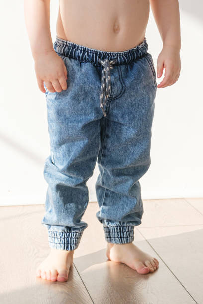 istock Barefoot toddler boy in elasticated jeans is standing on the floor 1476713796