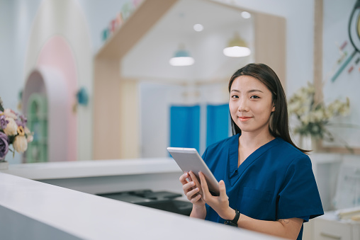 Retrato de una enfermera china asiática en el mostrador de la recepcionista del vestíbulo mirando a la cámara sonriendo photo