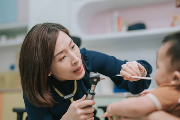 pédiatre chinoise d’origine asiatique examinant la gorge d’un bébé garçon avec un abaisse-langue dans sa clinique - doctor patient male tongue depressor photos et images de collection