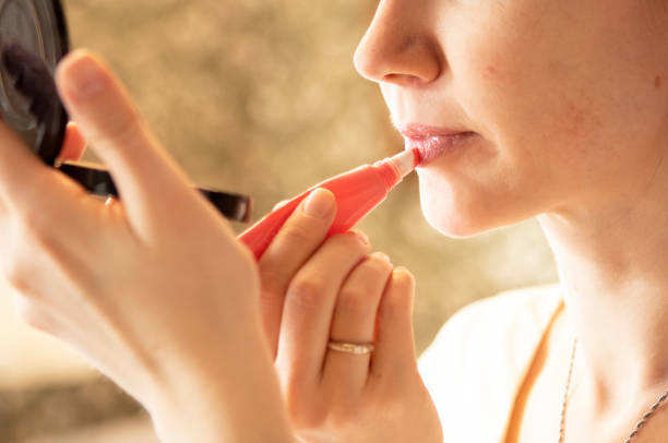 istock young girl paints her lips with gloss in front of a mirror 1476719454