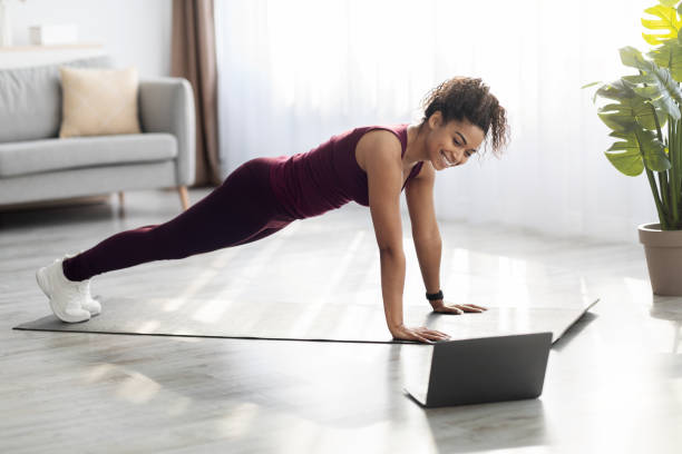 istock Positive slim african american woman exercising at home, using computer 1476719491