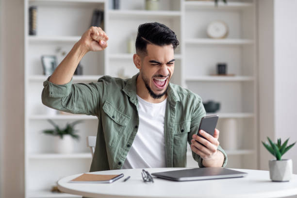 Great News. Overjoyed Young Arab Man Holding Smartphone And Celebrating Success stock photo