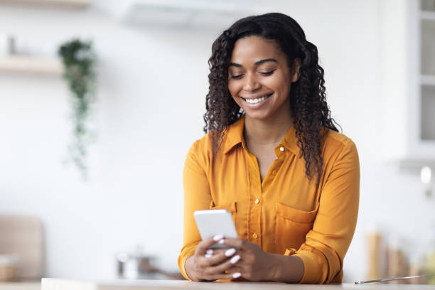 Cheerful black woman using brand new smartphone at home stock photo