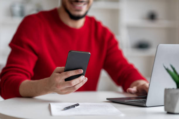 istock Arab Man Using Modern Mobile Phone While Sitting At Desk With Laptop 1476719708