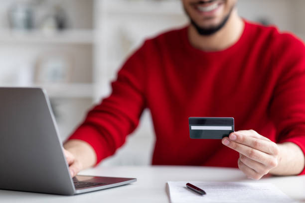 E-Commerce. Smiling Arab Man Using Laptop And Credit Card For Online Payments
