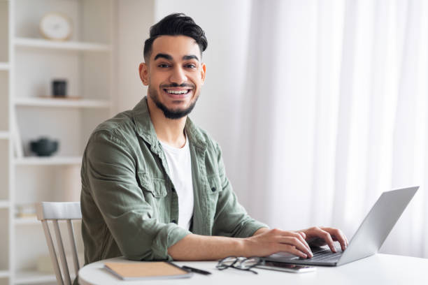 istock Smiling young islamic man manager with beard typing on laptop in home office interior, free space 1476720199