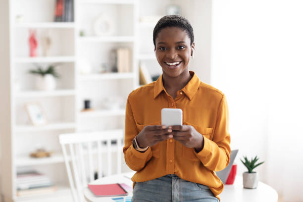 istock Positive young black woman with smartphone posing at workplace 1476720964