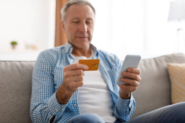 istock Mature man using phone and credit card at home 1476720992