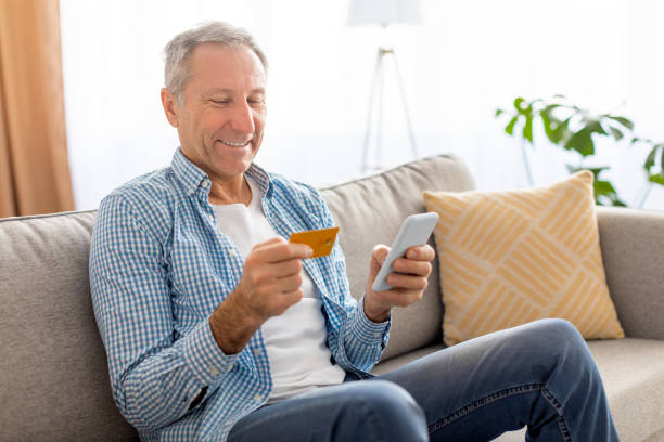 istock Mature man using cell phone and credit card at home 1476721010