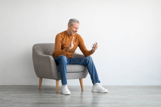 istock Smiling mature man waving hand using mobile phone 1476721328