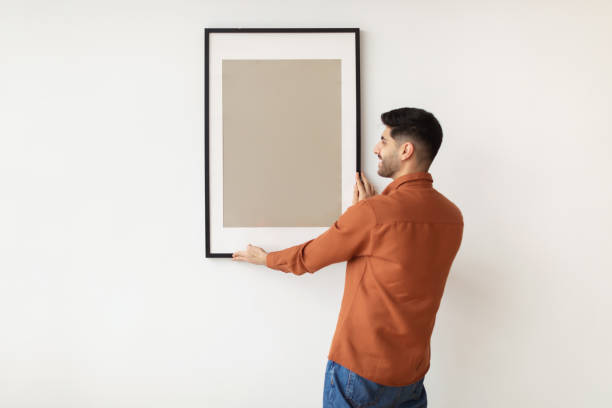 istock Young man hanging picture frame on the wall 1476722171