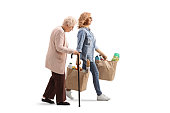 Full length profile shot of an elderly woman walking with a cane and younger woman carrying grocery bags