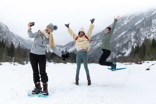 Friends on a hike through a snowy valley. They enjoy the vast landscape, the snow, play in the snow, take selfies for memories. Women's socializing, funny moments.\nMixed races.
