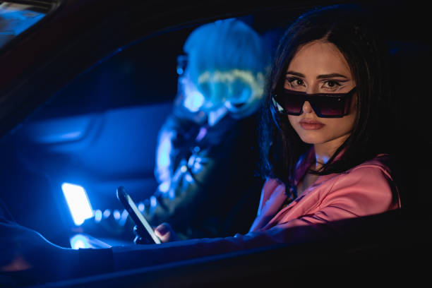 Female portrait of two women who wear futuristic glasses and using mobile phone indoors the car. Film Noir Style and cyberpunk concept photography, cinematic photo with neon light. Person with blue hairstyle, people and technology in vehicle. retrato femenino de dos mujeres que llevan gafas futuristas y utilizan el teléfono móvil en el interior del coche. film noir style y fotografía conceptual cyberpunk, foto cinematográfica con luz de neón. persona con peinado azul, personas y tecnologí