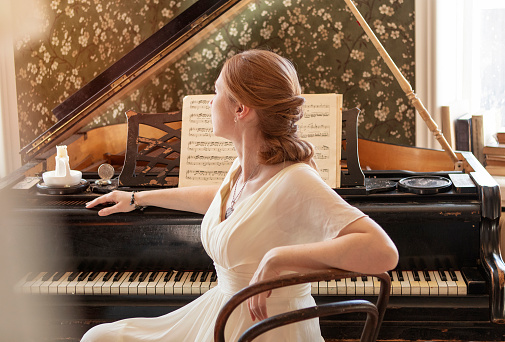 girl in a long white dress sits next to the piano