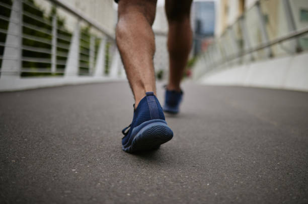 fitness, legs or runner walking on a city bridge in a warm for training, cardio exercise or calf muscle workout. wellness, zoom or sports athlete trekking or exercising with running shoes or footwear - snelwandelen stockfoto's en -beelden