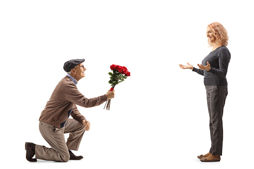 Senior man kneeling and giving a red roses to a woman isolated on white background
