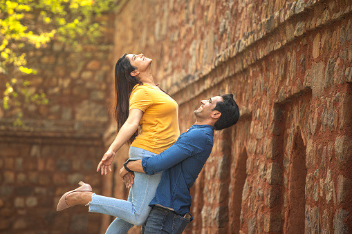 Happy loving man lifting up his girlfriend in the air during vacation at historic site