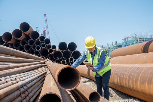 A female engineer uses a tablet computer to view steel pipes on a chemical plant site