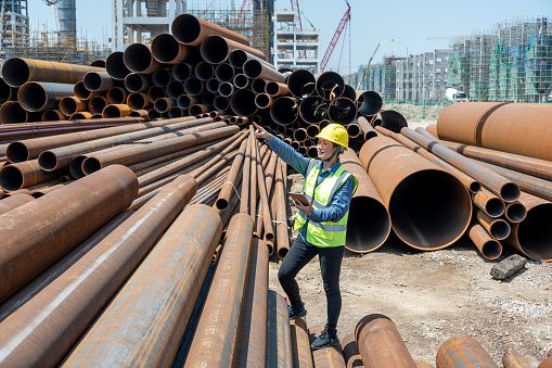 A female engineer uses a tablet computer to view steel pipes on a chemical plant site