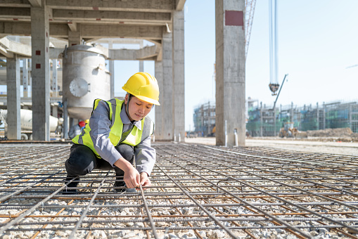 A confident female worker is binding steel bars on a construction site