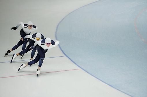 Row of three young active athletes on skates sliding along ice rink while practicing some exercises during training before competition