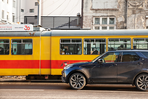 Picture of a belgrade tram in the city center of Belgrade, Serbia, sharing the road with a luxury SUV. The Belgrade tram system is a 1000 mm gauge network that in 2011 had 10 routes running on 43.5 kilometres of track in the city of Belgrade, the capital of Serbia.