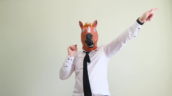 A man in a horse mask dances on the background in the studio. A funny dance performed by a man.