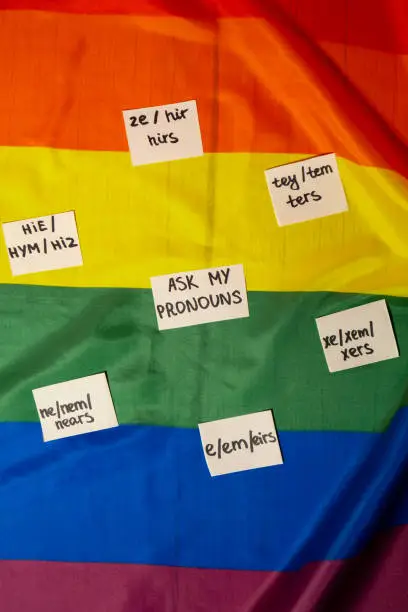 ASK MY PRONOUN Neo pronouns concept. Rainbow flag with paper notes text gender pronouns hie, e, ne, xe, ze, tey. Non-binary people rights transgenders. Lgbtq community support assume my gender, respect pronouns tolerance equal rights