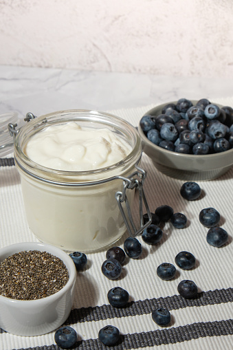 Glass jar with natural organic homemade yogurt and blueberries chia seeds pudding. Immunity-boosting ingredients. Concept of healthy eating breakfast of Greek yogurt in glass jar and fresh blueberries on white concrete background. Fermenting superfood