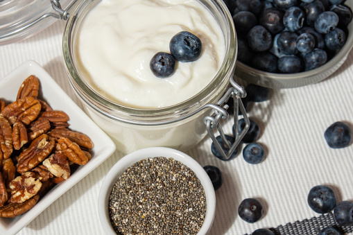 Glass jar with natural organic homemade yogurt and blueberries pecan nut chia seeds pudding. Immunity-boosting ingredients. Concept of healthy eating breakfast of Greek yogurt in glass jar and fresh blueberries on white concrete background. Fermenting superfood