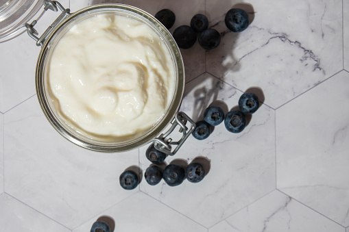 Glass jar with natural organic homemade yogurt and blueberries on table. Immunity-boosting ingredients. Concept of healthy eating breakfast of Greek yogurt in glass jar and fresh blueberries on white concrete background. Fermenting superfood