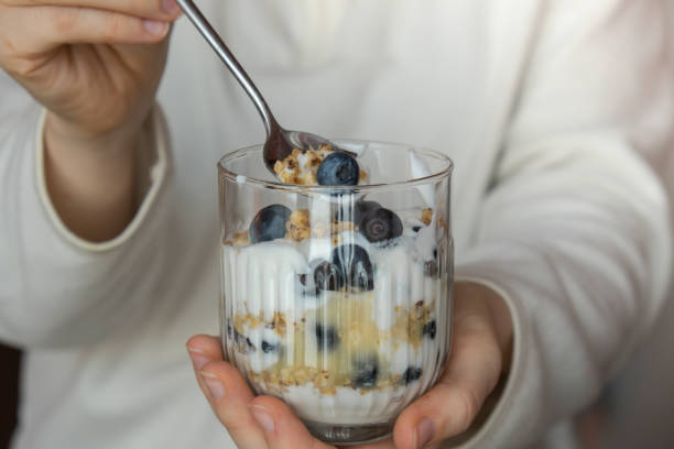 Unrecognizable woman eating Morning granola breakfast with homemade greek yogurt, blueberries in glasses on blue wooden background. Healthy diet Crunchy granola with yogurt nuts and blueberries Unrecognizable woman eating Morning granola breakfast with homemade greek yogurt, blueberries in glasses on blue wooden background. Healthy diet Crunchy granola with yogurt nuts and blueberries for healthy light breakfast eating chia seeds stock pictures, royalty-free photos & images
