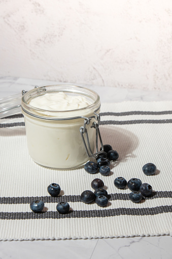 Glass jar with natural organic homemade yogurt and blueberries on table. Immunity-boosting ingredients. Concept of healthy eating breakfast of Greek yogurt in glass jar and fresh blueberries on white concrete background. Fermenting superfood