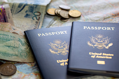 two US American passports laying on large road map of foreign country close-up with foreign currency bills and coins Illustrative editorial 3/25/23 Newnan, GA, map Laufzeit 1991-1993