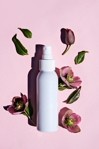 White plastic bottle and natural flowers on a pink background. Cosmetics for body and face care. Vertical image.