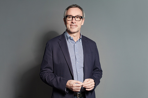 Portrait of happy cheerful mature businessman in blue suit, checked shirt and glasses against grey studio  background
