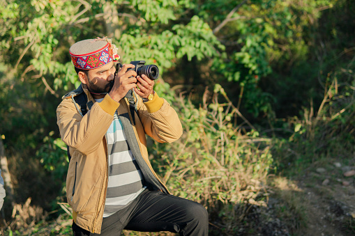 young man taking photographs with a camera while tracking and exploring in the mountain forest.