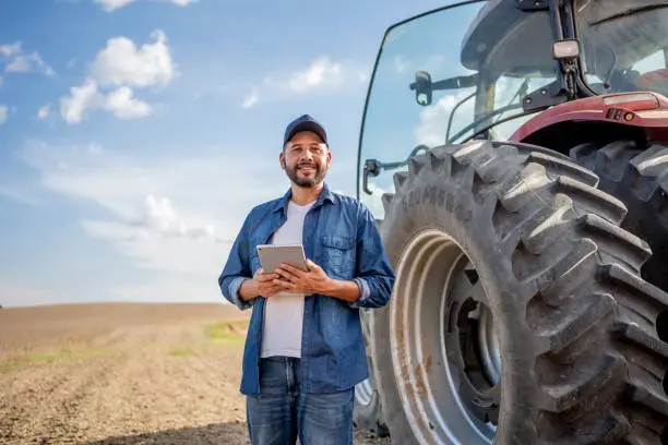 Photo of Portrait of farmer with tablet in front of his tractor