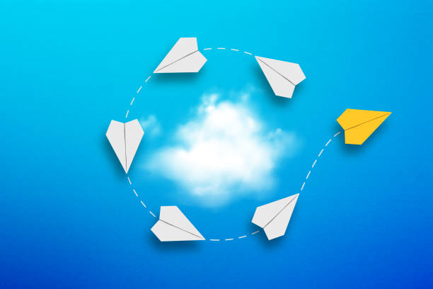 istock Different business concept. Yellow paper airplane separating from white paper airplanes orbiting around a white cloud. 1476758832