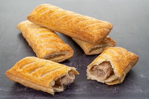 Sausage rolls with one sliced open on a dark background