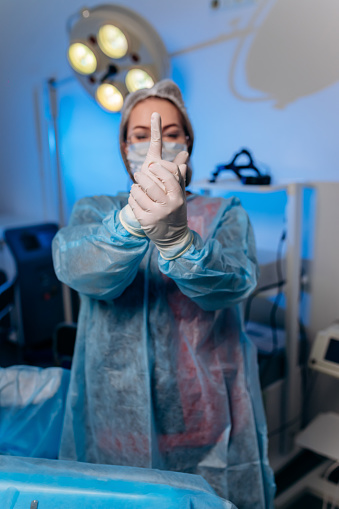 Proctóloga vestida con uniforme médico posa mostrando dedos y sonriendo en el hospital antes de la operación photo