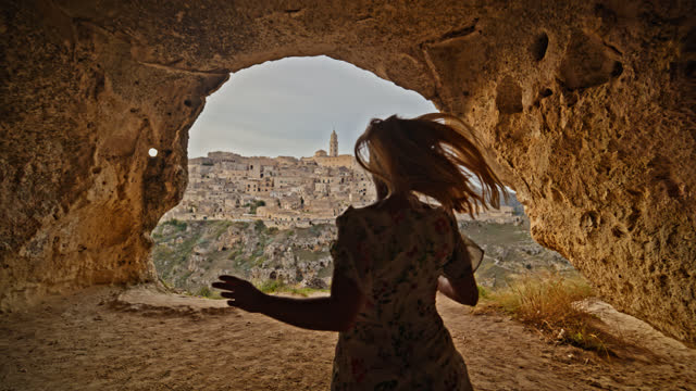 Slow motion of woman running in arched cave at Sassi di Matera. A woman is having fun on a trip around Italy.