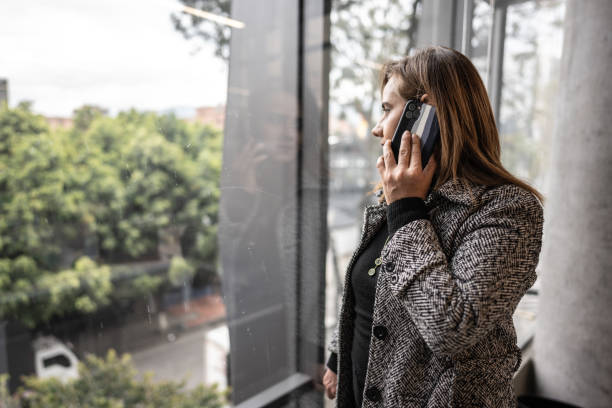 istock Mature woman talking on phone while looking through window at office 1476764608