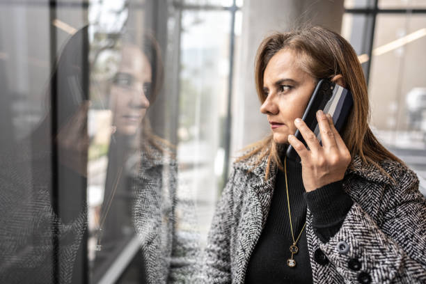 istock Mature woman talking on phone while looking through window at office 1476764609