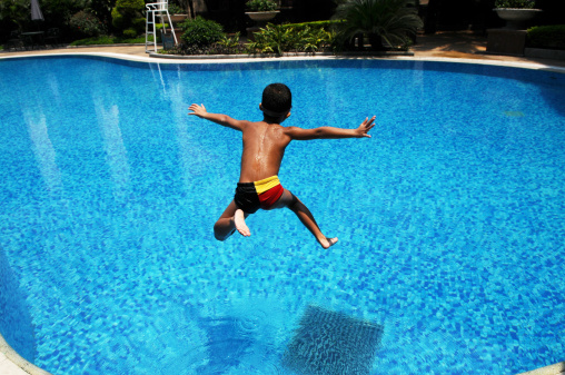A Chinese little boy jumps into the blue,clear water in a swimming pool for cool in a hot summer day.