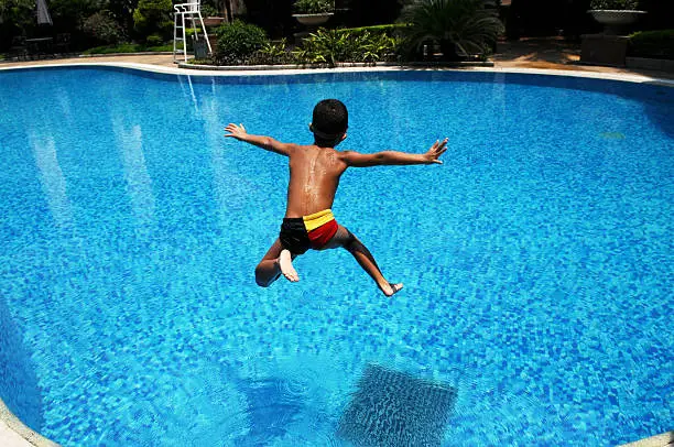 A Chinese little boy jumps into the blue,clear water in a swimming pool for cool in a hot summer day.