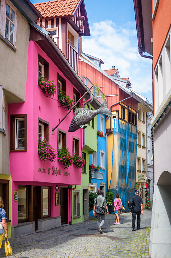 Street with colored houses in old town of Lindau, Germany. People walk down lane past shops and restaurants in summer. This city is tourist attraction of Bavaria.