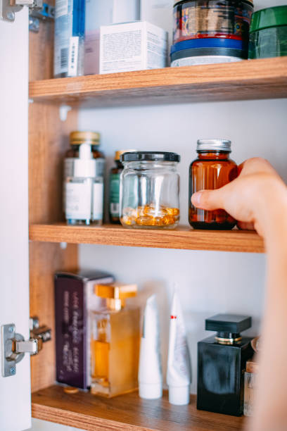 mujer tomando vitaminas del gabinete del baño - armario de aseo personal fotografías e imágenes de stock